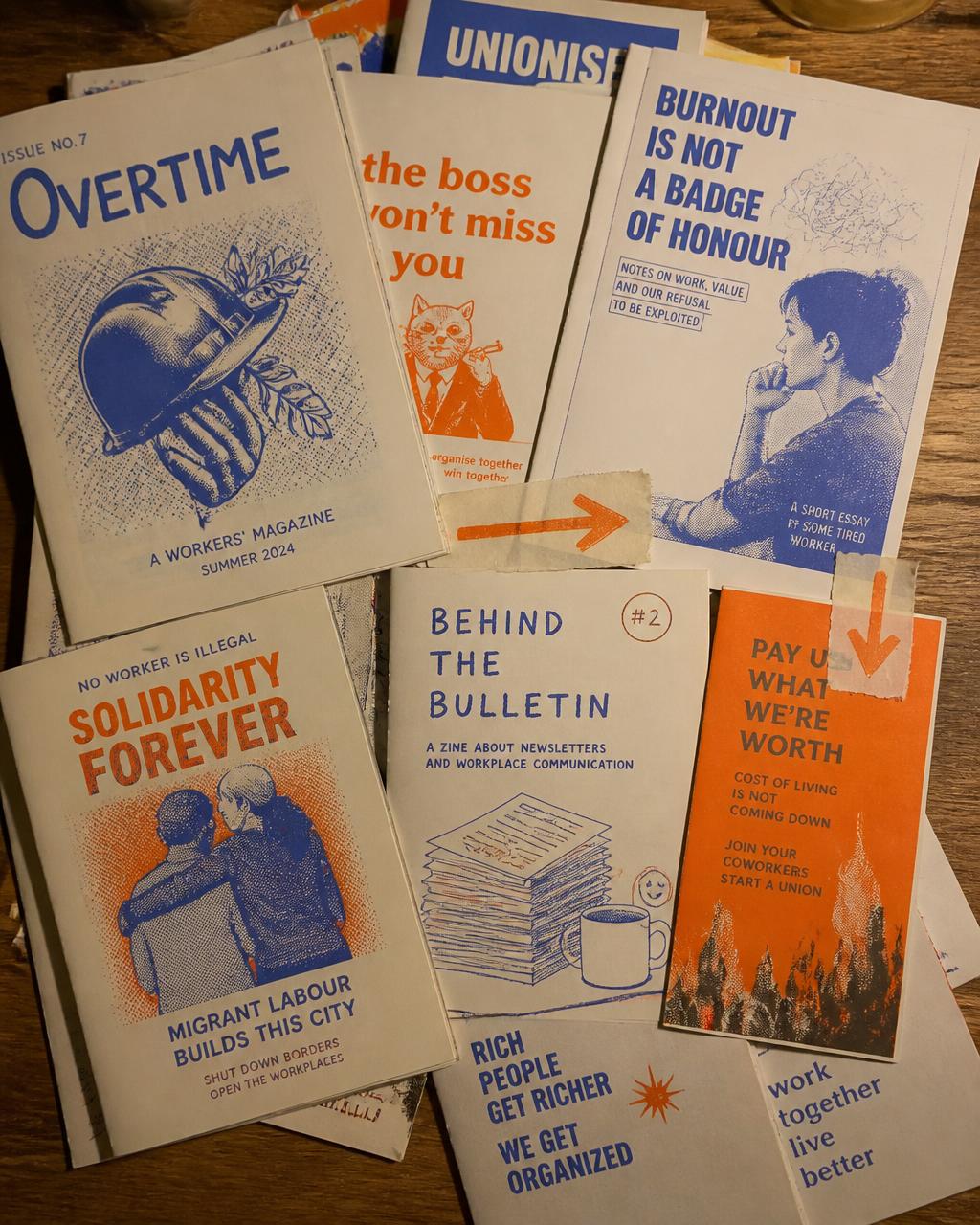 A messy stack of risograph zines and labour flyers on a wooden table
